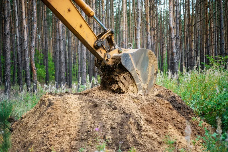 Excavator bucket digging earth during an excavation and trenching job on a rural property in Shelby County, Indiana