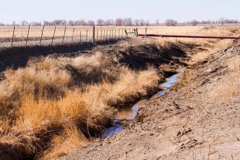 Rural drainage ditch carrying water alongside a fence line and farm field in central Indiana